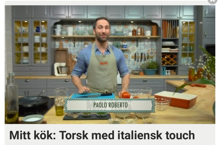 Kock i förkläde leende i kök framför ingredienser för att tillaga torsk med italiensk touch.