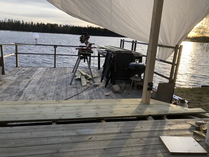 Byggplats för ett uterum med verktyg och material, stolpar uppsatta, vid en sjö i skymningen.