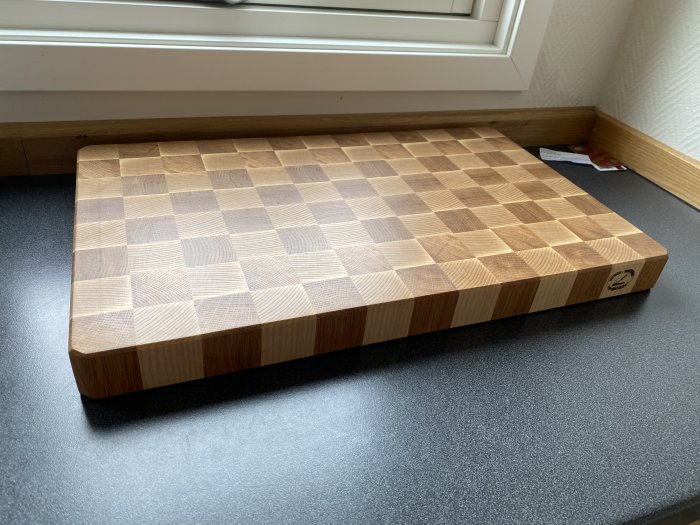 Handtillverkad skärbräda i ek och ask med schackrutigt mönster, placerad på ett köksbord.