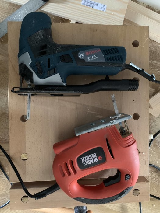 Två sticksågar, en nyare Bosch-modell ovanpå en äldre Black & Decker, ligger på en träplanka.