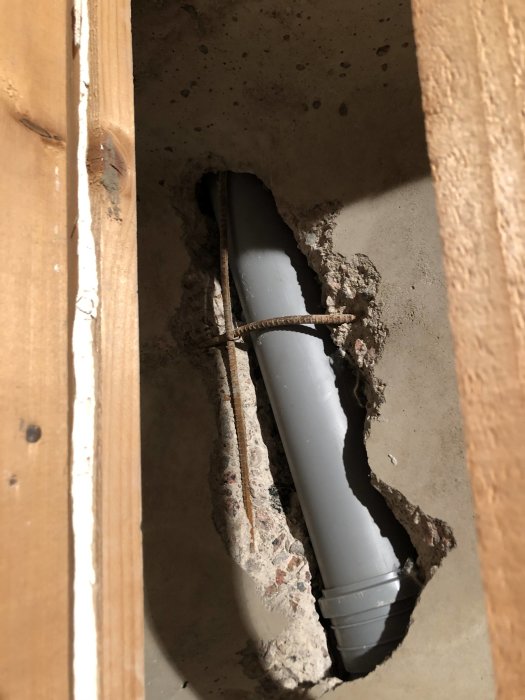 Öppning i ett rivet gipstak som avslöjar ett avloppsrör omgivet av betong och skräp.