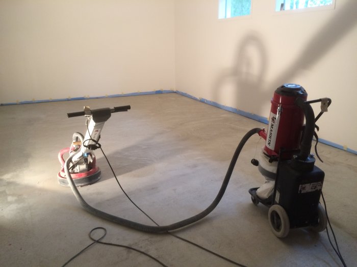 Golvslipningsmaskiner på avslipat betonggolv för förberedelse av trägolvsinstallation.