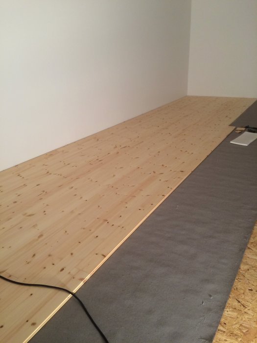 Installation av flytande furuträgolv över OSB-skivor och byggplast på slipat betonggolv.
