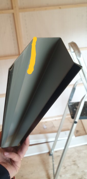 Hand håller en vinklad metallplåt markerad för kapning för anpassning mot trekantslist.