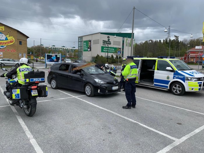 Svensk polis på parkeringsplats med motorcykel och polisbil under dagtid.