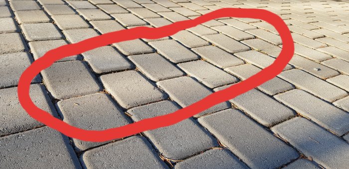 Gatsten som sjunkit ner markerat med röd cirkel på en trottoar.