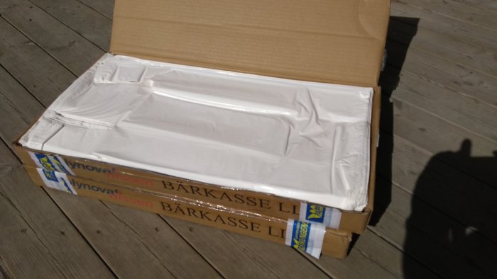 En kartong med en stor mängd hopviktade vita plastpåsar på en träterrass.