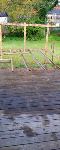 Plintar och reglar monterade på en pågående trädgårdsrenovering, med staketstolpar och en delvis byggd ramverksstruktur.