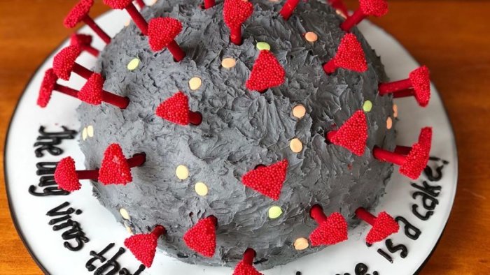 Tårta dekorerad för att efterlikna coronaviruset med röda toppingar och skrift på fatet.