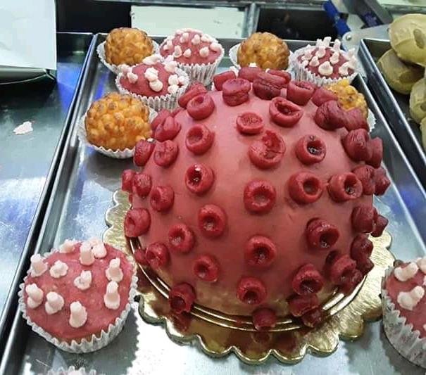 Tårta dekorerad för att likna ett coronavirus, omgiven av mindre bakelser på ett serveringsfat.