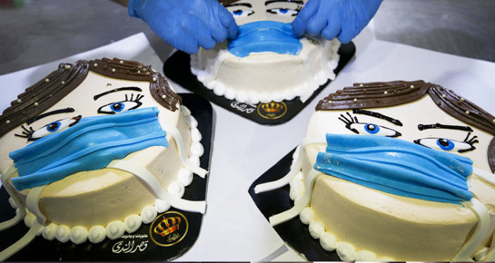 Tårtor formade som ansikten med munskydd, handsklädde händer justerar masken på en tårta.