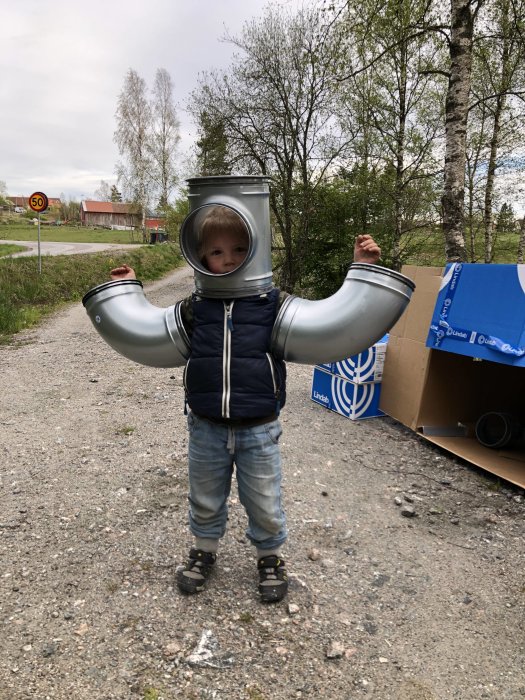 Barn i jacka och jeans som leker med stora ventilationsrör ute på en grusväg.