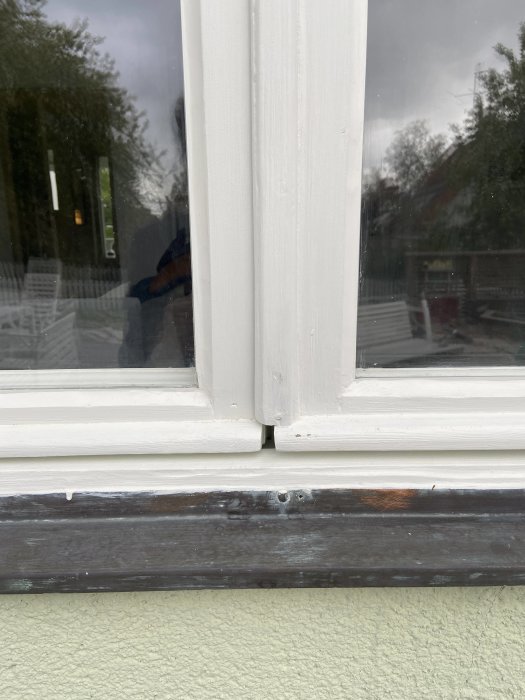 Mellanrum där två fönsterdelar möts, med synligt slitage och fuktmärken på trälisten.