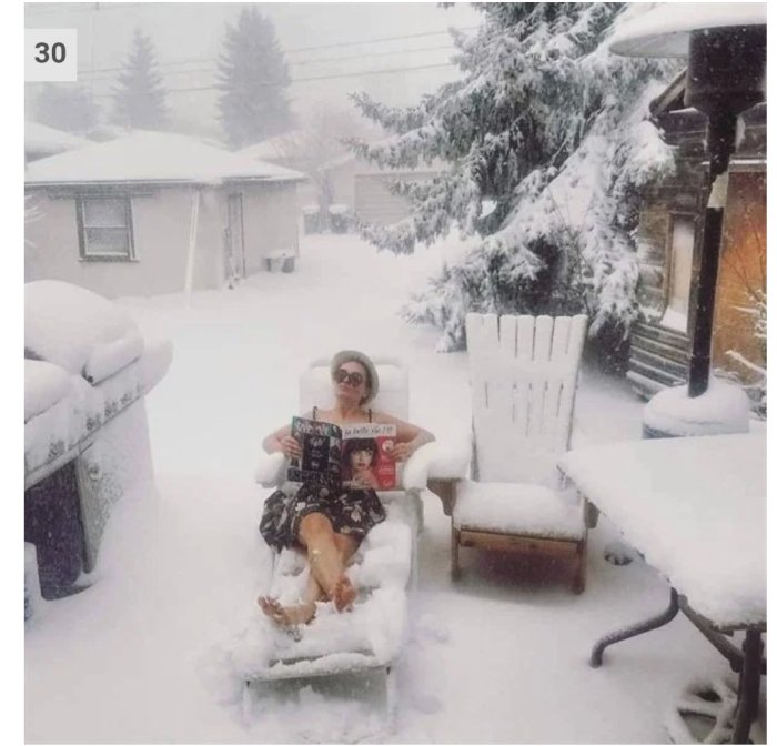 Person i solglasögon och sommarkläder sitter i snötäckt trädgårdsstol och läser en tidning.