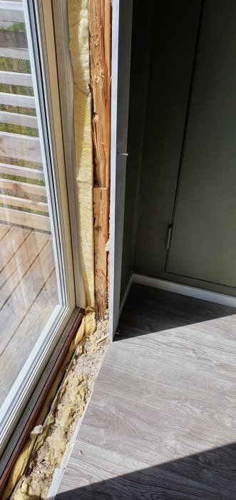 Nyinstallerat fönster med synlig isolering och en glipa mellan fönsterkarm och Ett oavslutat golv som inte når fönsterkarmen.