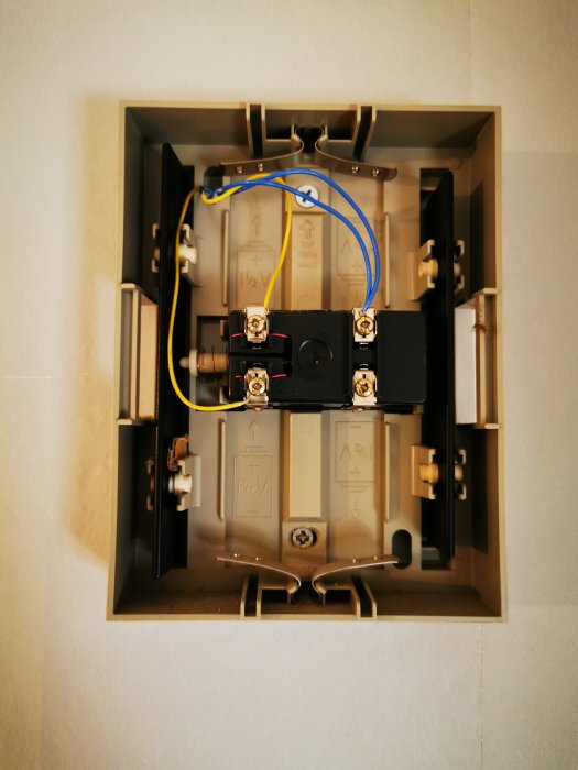 Öppen elektrisk dosa med oanslutna kablar och installationselement på en vägg.