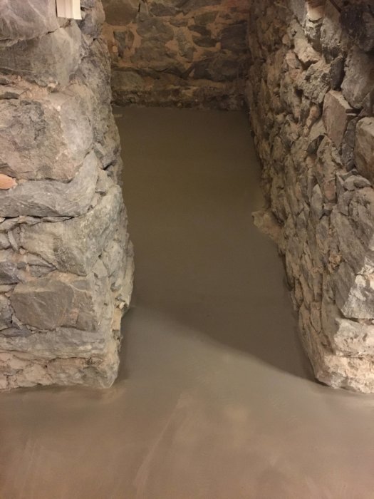 Nyligen lagt andra lagret av betong på ett källargolv med stenväggar runtomkring.