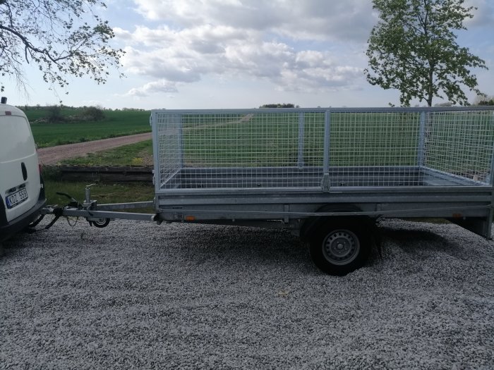 Nytt Brenderup D1000 släpvagn med galler kopplat till en vit bil, parkerat på grusunderlag.