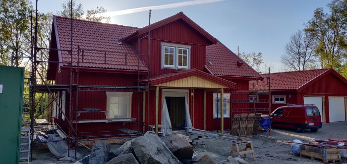 Rödmålat hus under renovering med byggnadsställningar och oavslutad fasad.