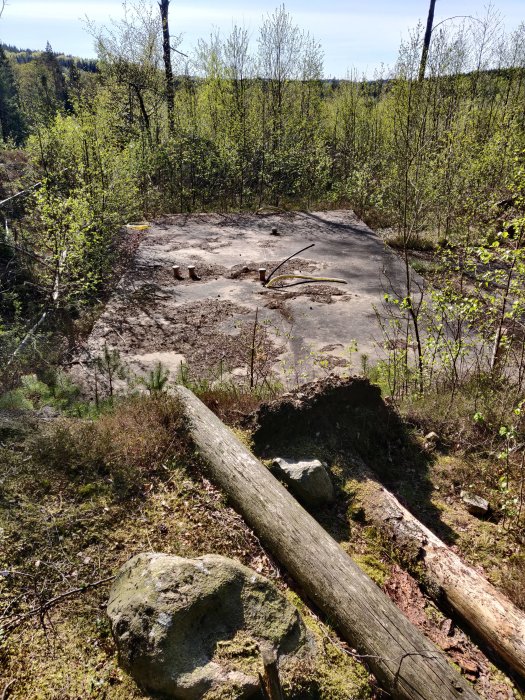 Betongplatta på en tomt omgiven av grönska och träd, med synliga tecken på förfall och spruckna kanter.