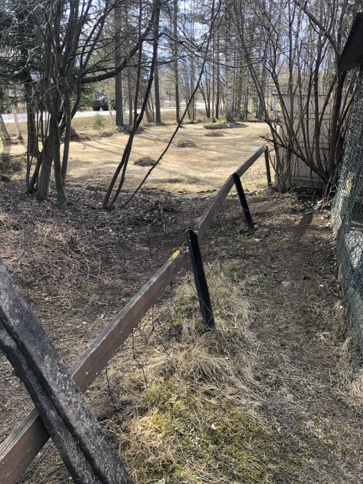 Gamla sneda trästaket med metallstolpar i betongplintar på en övergiven gård.