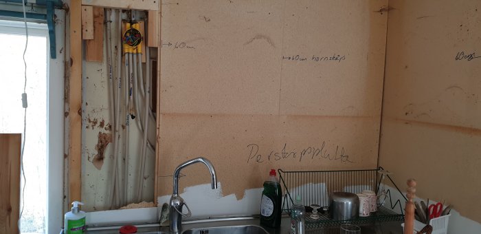 Köksvägg efter borttagning av 70-tals skåp med exponerade reglar, spånskiva och elledningar.