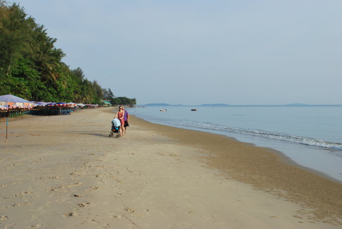 Strand i Mae Phim, Thailand med lagom med folk, par promenerar bredvid havet, parasoller i bakgrunden.