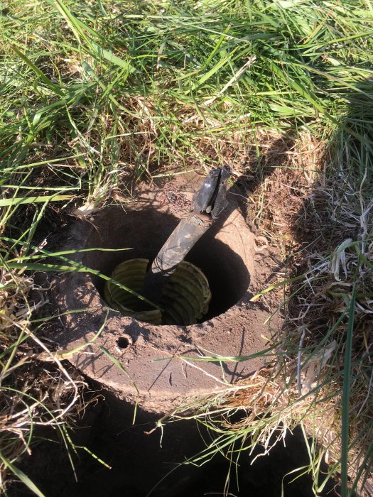 Bild på öppnat fundament med befintligt elrör i marken, synliga skador, omgiven av gräs och jord.