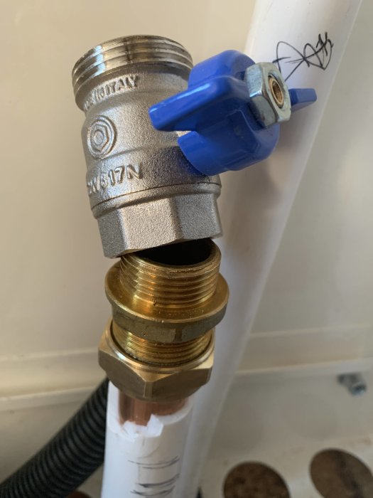 Avstängningsventil med blå spak kopplad till en rörinstallation med gängade metallfogar.