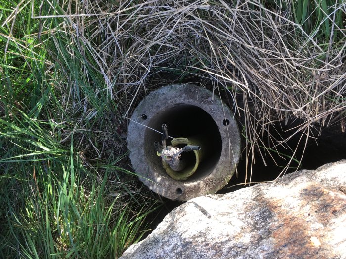 Betongrör i mark med skadad elektrisk kabel och gräs runt öppningen, använd för pollarens fundament.