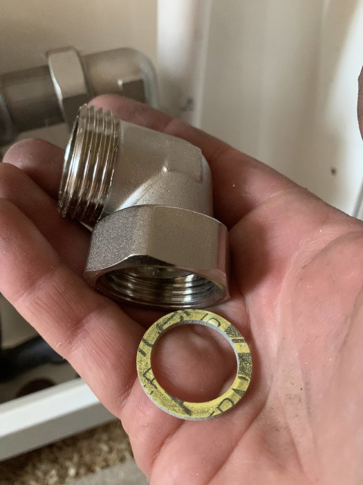 Hand håller en metallvinkelkoppling och en fiberpackning inom VVS.