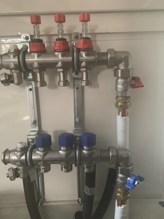 Installation av rör med flera ventiler, två blå pekar åt höger, en röd delvis synlig i övre högra hörnet.
