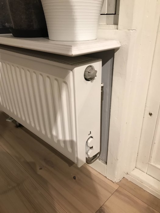 Radiator med synlig värmekoppling och skadat golv, som tyder på tidigare läckage vid radiatorn.