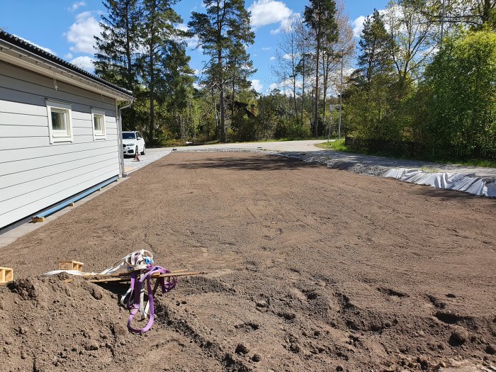 Nyjordad yta bredvid huset förberedd för att anlägga gräsmatta, kratta i förgrunden.