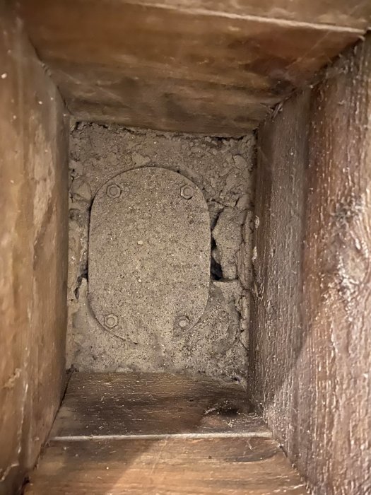 Betonglock i en potentiell rensbrunn inne i en träinramad öppning på ett golv.