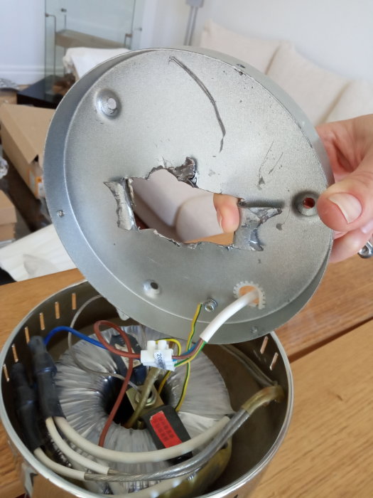 Hand som håller en taklampans metallfäste med utvidgat hål och synliga kablar och lampdelar inuti.