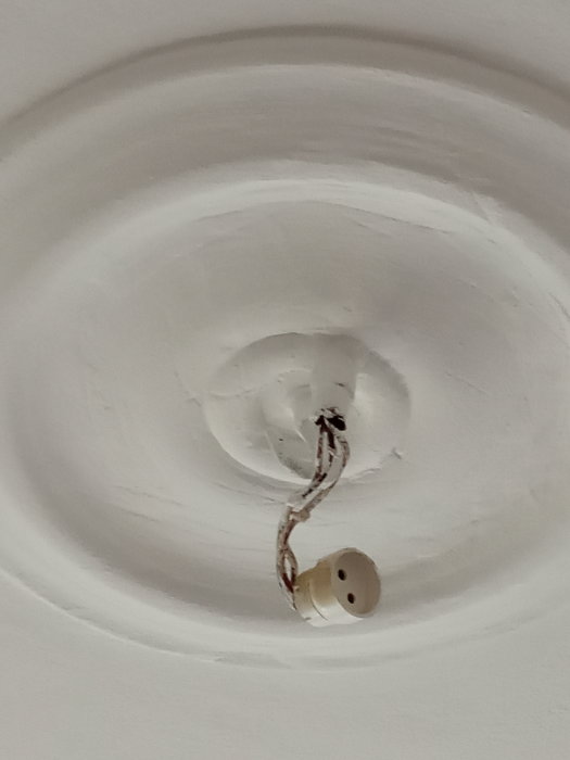 Taktillfälle med utstickande elektriska kablar och en gammal krok i ett sekelskifteshus med vitmålade runda dekorationer.