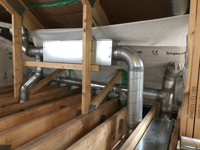 Ventilationsrör och isolering installerade i trång kattvind med tejpade skarvar.