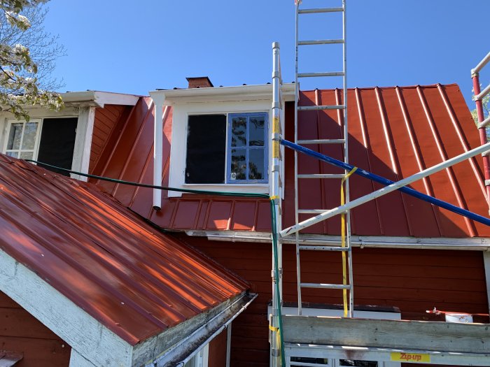 Nyrenoverat rött tak på ett hus med byggställningar och stege, under en klarblå himmel.