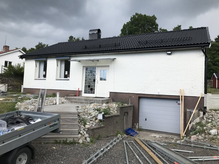 Renoverat hus med nytt svart tak, fasadbelysning och byggmaterial framför.