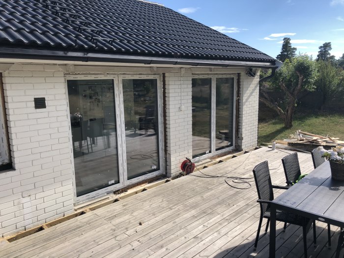 Nyinstallerade fönster och terrassdörrar på en vitteglad husfasad med en trätrallveranda och byggmaterial synligt.