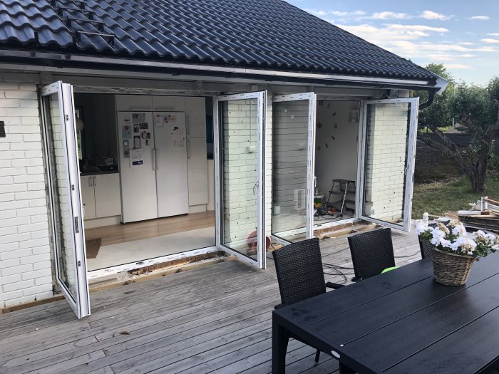 Nyinstallerade vita fönsterpartier på ett hus med öppna dörrar som visar insidan från en trädäckad uteplats.