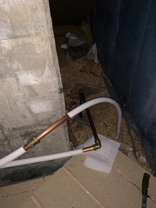 Rörinstallation med kopparfördelare och vita plaströr i ett oordnat utrymme med siktbara skarvar.