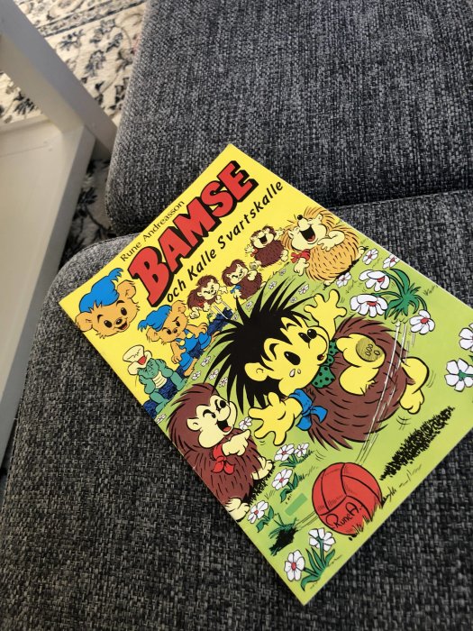 Bamse-tidning med titeln "Bamse och Kalle Svartskalle" som ligger på grå sofftyg.