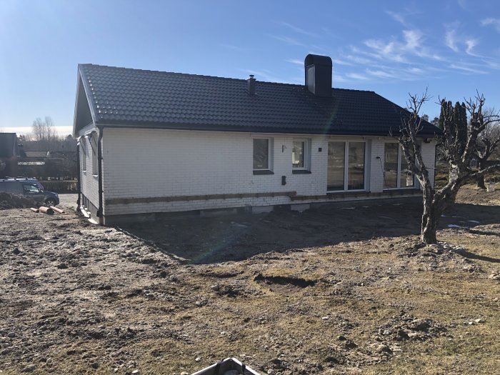 Enfamiljshus och en rörig, gräsfri tomt i starkt solljus.