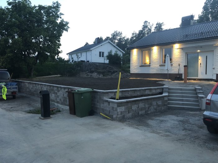 Nybyggd stödmur och avloppsränna vid garage på en tomt under kvällsljus.