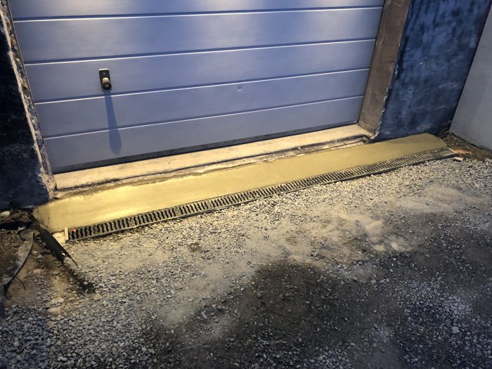 Nyinstallerad ränna längs garageport med betongstödmurar och grusunderlag.