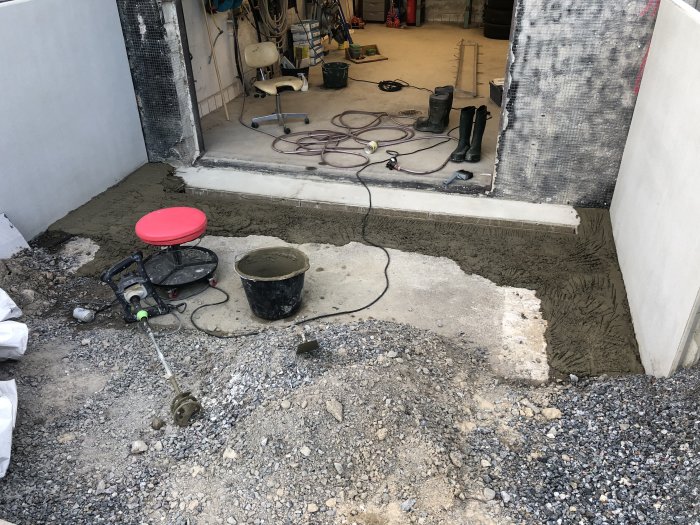 Renoveringsarbete vid garageinfart med nyligen gjuten betong, verktyg och byggmaterial synliga.