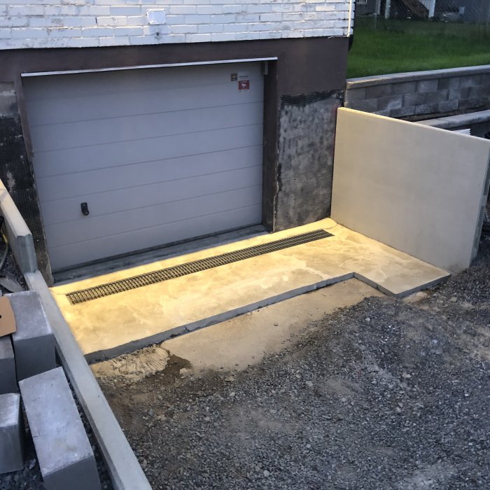 Renoverad garageinfart med ny gallerdurk och betongram, armeringsnät synligt, ovädersskydd.