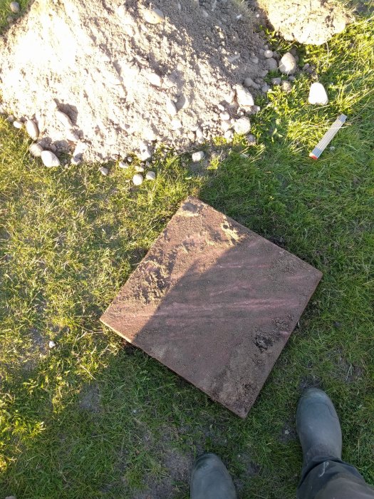 Bild på ett stort betonglock i en trädgård som markering för en gammal brunn, omgivet av gräs och grus.